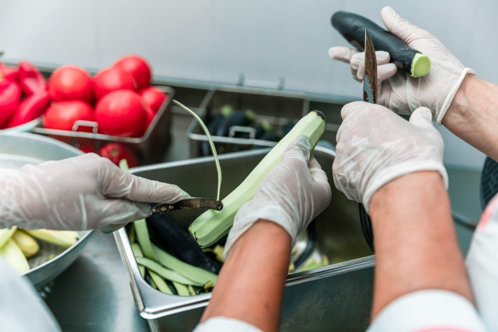 Mains gantées parant des légumes frais au-dessus des bacs inox d’une cuisine professionnelle